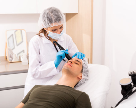 Young man getting needleless mesotherapy for face at beauty clinic