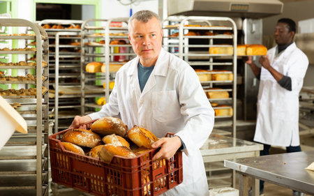 Confident bakery worker carrying plastic box with freshly baked loaves