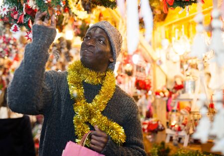 Smiling African American man selecting festive home decoration at outdoor Christmas fairの写真素材
