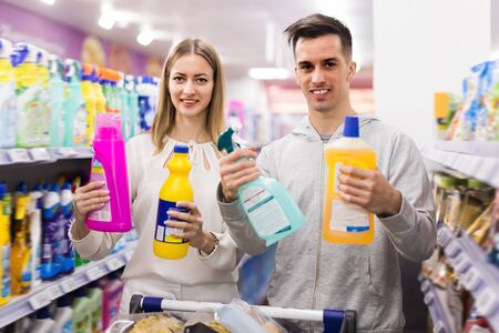 Fine couple doing shopping together, choosing household detergents in storeの写真素材
