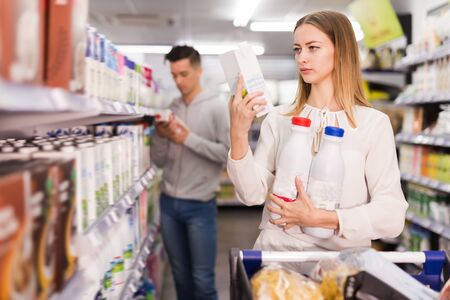 Smiling female customer choosing milk and dairy products in groceryの写真素材