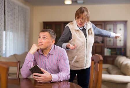 Frustrated adult man listening to reprimanding from his elderly mother at homeの写真素材