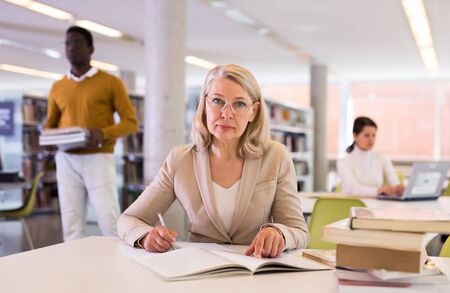 Portrait of successful teacher woman with book in public libraryの写真素材