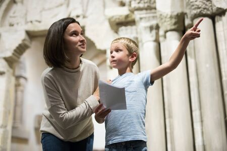 Young woman with son observing with interest sculptures exhibition in art museum, pointing to something interestingの写真素材