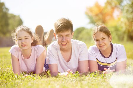 Group of positive teenagers lying on green grass in parkの写真素材