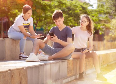 Company of teenagers with smartphones are communicating on walk in the cityの写真素材