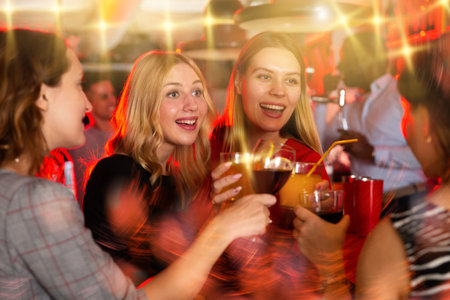 Chatting friends holding cocktails and laughing in nightclub