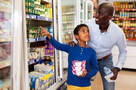 Happy friendly  positive  African family of father and tween son shopping together in supermarketの写真素材