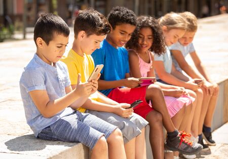 Kids using phones outdoors, concept of children addiction to social networkの写真素材