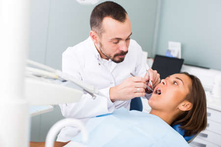 Dentist is treating patient which is sitting in dental chair in clinicの写真素材