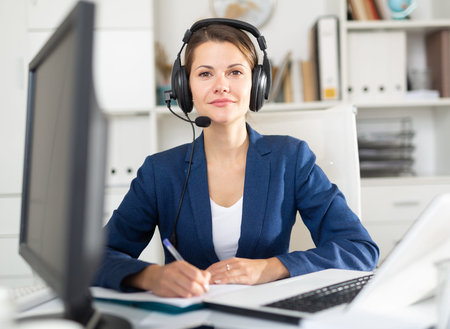 Office worker woman is working at a computer and talking by headset with client