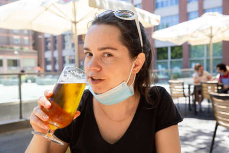 Woman in protective medical mask with glass of beer at barの写真素材