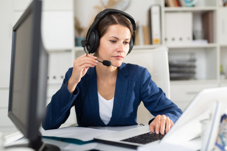 Office worker woman is working at a computer and talking by headset with client