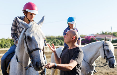 Trainer talking to woman while riding horse at farm