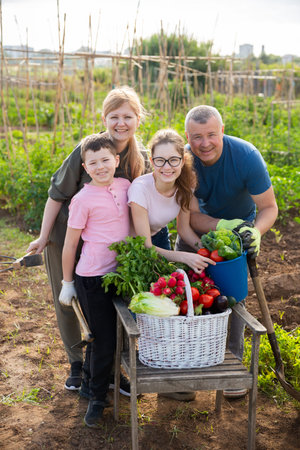 Cheerful family holding vegetables grown in home garden