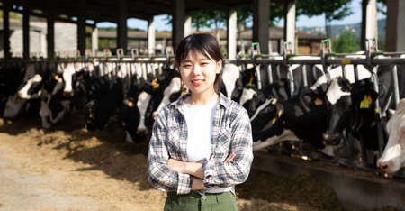 Positive female farmer who is standing near cows at the farmの写真素材
