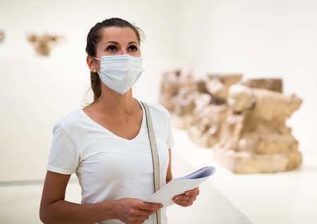 Woman in mask exploring sculptures in galleryの写真素材