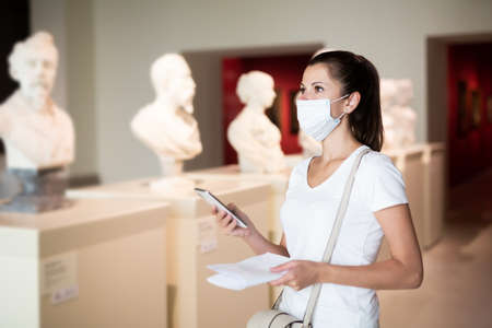 Woman in mask observing sculptures using phoneの写真素材