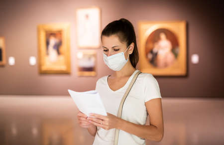 Woman in mask observing artworks in museumの写真素材
