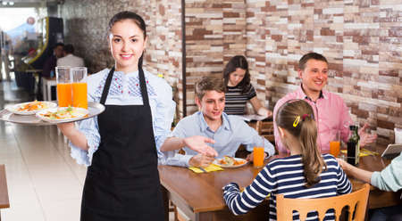 Adult female is ready to serve salad and juice to young visitorsの写真素材