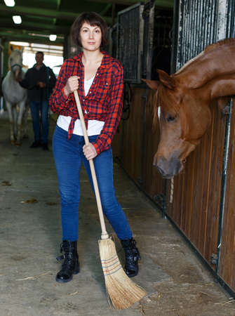 Woman horse farm worker cleaning floorの写真素材