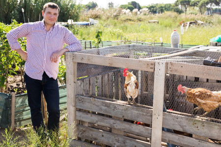 Positive male proffesional farmer standing near chicken house