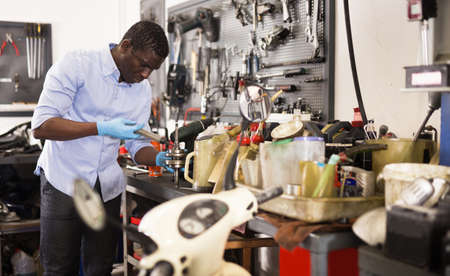 Confident worker examines a broken motorcycle part of the working areaの写真素材