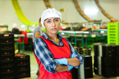 Portrait of female worker in uniform with arms crossed standing in warehouseの写真素材