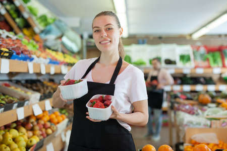 Young woman seller standing with small boxes of strawberryの写真素材
