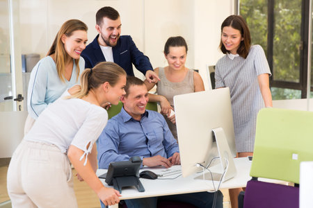 Happy young business men and females talking around computer monitor