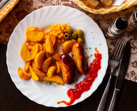 Grilled sausages served with potatoes, olives and chili sauceの写真素材