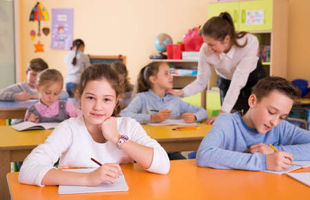 Pupils sitting at lesson, woman teacher helpingの写真素材