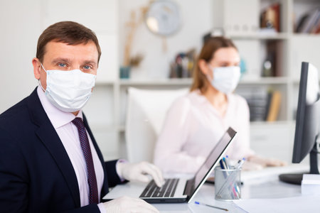 Businessman in face mask working with female assistant in office