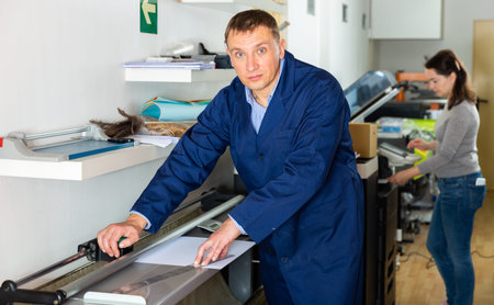 Printing employee cuts paper on a roller cutter machine