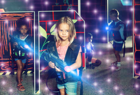 Smiling girl aiming laser gun at other players during lasertag game in dark roomの写真素材