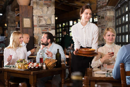 Young female waiter serving country restaurant guestsの写真素材