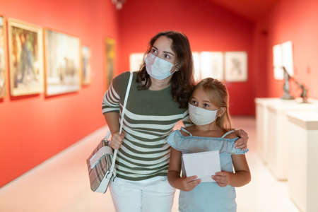 Mother and daughter in protective medical masks looking at expositions in museumの写真素材