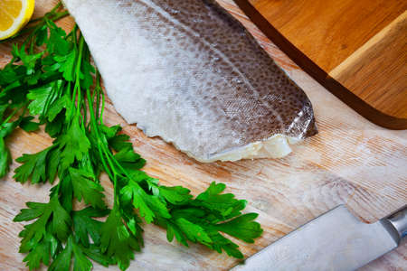 Fillet of raw codfish on a wooden surface with garlic and greensの写真素材