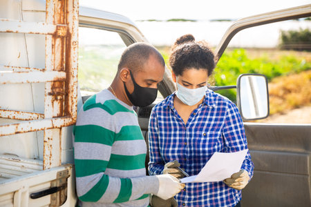 Delivery courier in protective masks invites the farmer to sign documents on the field