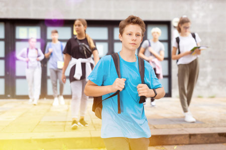 Teen boy walking to college campus in autumn day