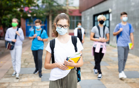 Teenage girl in protective mask with a backpack and notebooks walking in the street