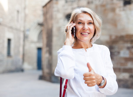 Smiling mature woman talking on phone and thumb up