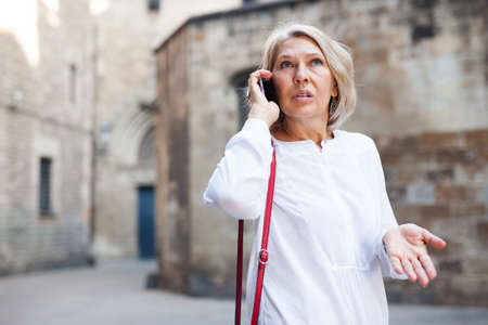 Adult female is talking by phone with friend on the street outdoorの写真素材