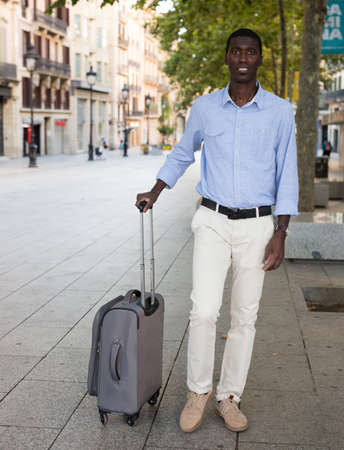 Portrait of an african american tourist on the street of city with suitcaseの写真素材