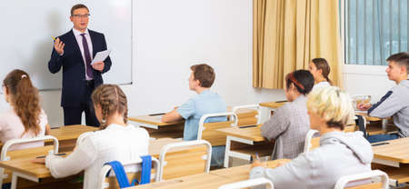 Man teacher with notebook is giving interesting lecture for students in classroom