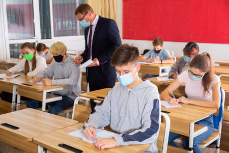 Teacher man in protective mask helping students during lesson