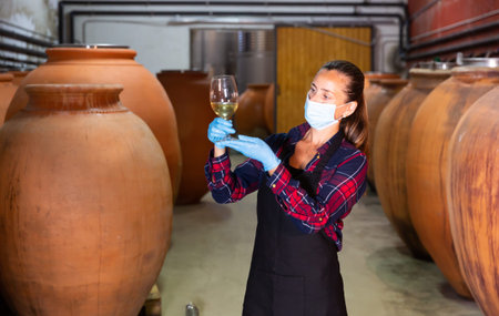 Female wine worker in a protective mask checking quality of product