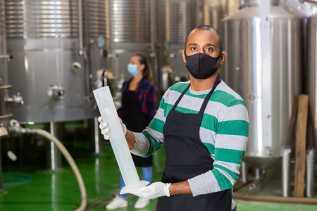 Winemaker in mask checking wine at factory
