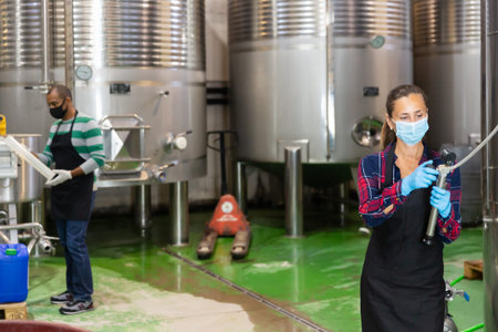 Winery workers in protective masks control wine production process