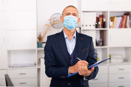 Portrait of business man in protective mask with folder of documents at officeの写真素材